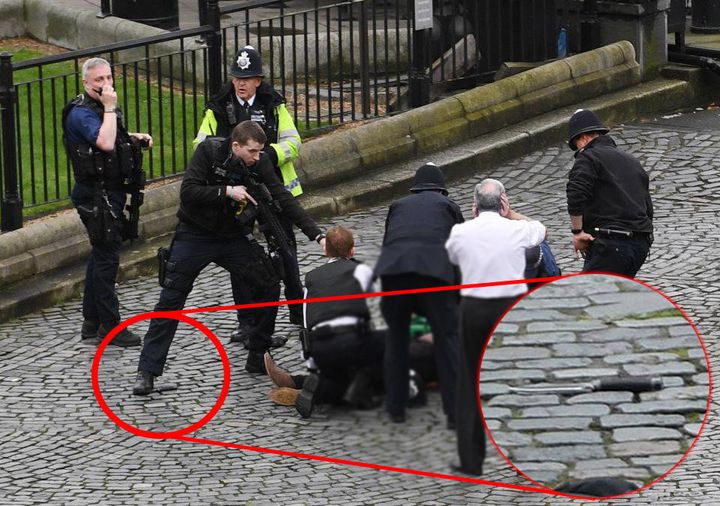A police officer stands on top of a knife while aiming his gun at the suspected attacker outside Parliament