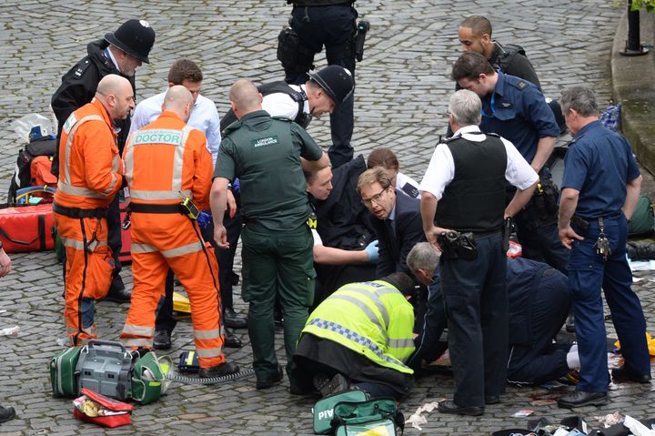 Conservative MP Tobias Ellwood (centre) helps emergency services attend to a police officer outside the Palace of Westminster.