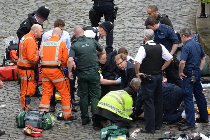 Conservative MP Tobias Ellwood (centre) helps emergency services attend to a police officer outside the Palace of Westminster.