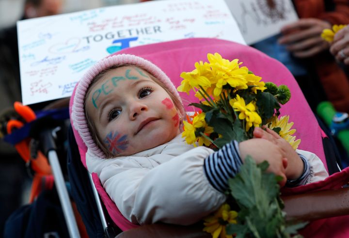 A baby holds a bunch of flowers at the vigil