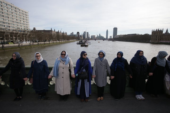 Women activists wearing blue hold hands on Westminster Bridge in front of the Houses of Parliament to honour the victims of t