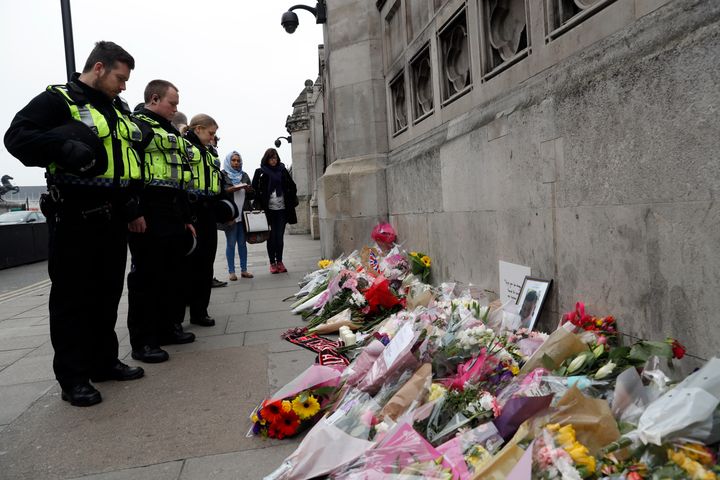 Police officers and civilians look at floral tributes near Westminster Bridge following a recent attack in Westminster.