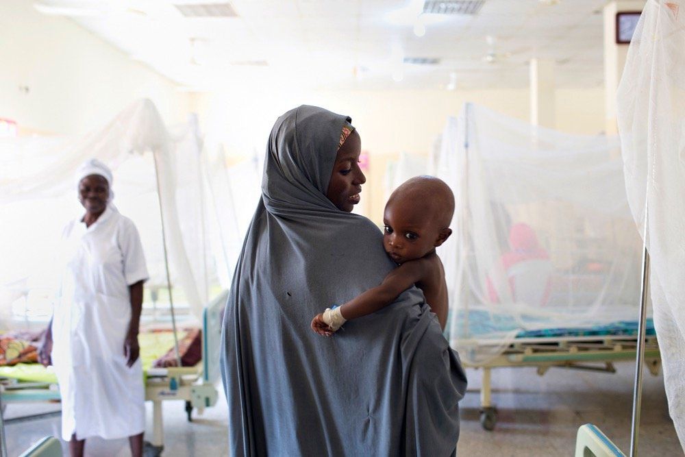 A mother carries her child, who suffers from severe acute malnutrition, through an inpatient stabilization center run by the IRC in Maiduguri.
