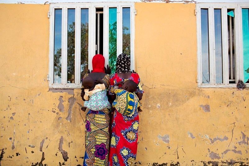 Women watch as people carry food supplies out of a storage building at the Fufore camp for internally displaced persons outside of Yola in northeastern Nigeria’s Adamawa State.