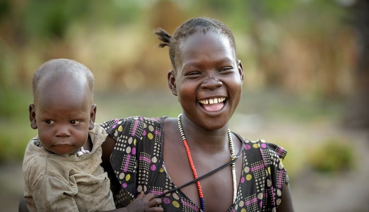 Mother and baby watch as other community members water their vegetable gardens in Kuajok, Warrup State, South Sudan.