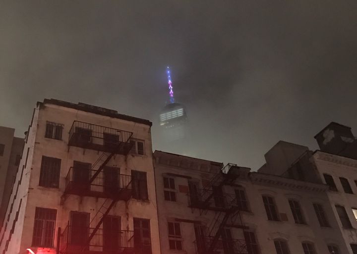 One World Trade Center lit in the trans colors against a foggy sky, as seen from Chambers Street.