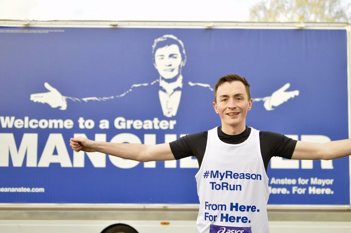 Sean Anstee poses in front of a billboard at the Greater Manchester Marathon