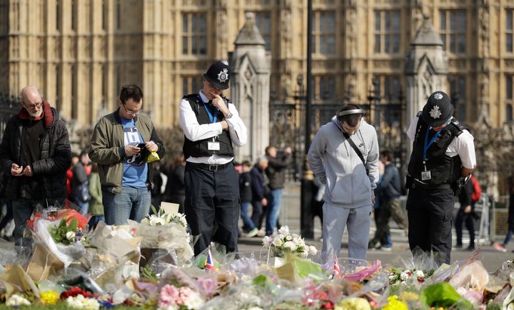 Police officers and members of the public look at the floral tributes to the victims of the Westminster attack placed outside the Palace of Westminster