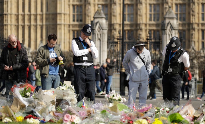 Police officers and members of the public look at the floral tributes to the victims of the Westminster attack placed outside the Palace of Westminster