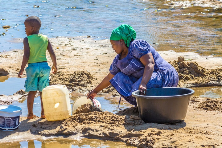 South Africa - August 24, 2014: African woman with child collecting water from the river on the road leading to local Game Reserve.