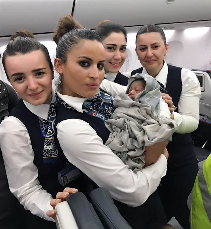 Four members of Turkish Airlines staff are seen welcoming an unexpected passenger following a mid-flight delivery.