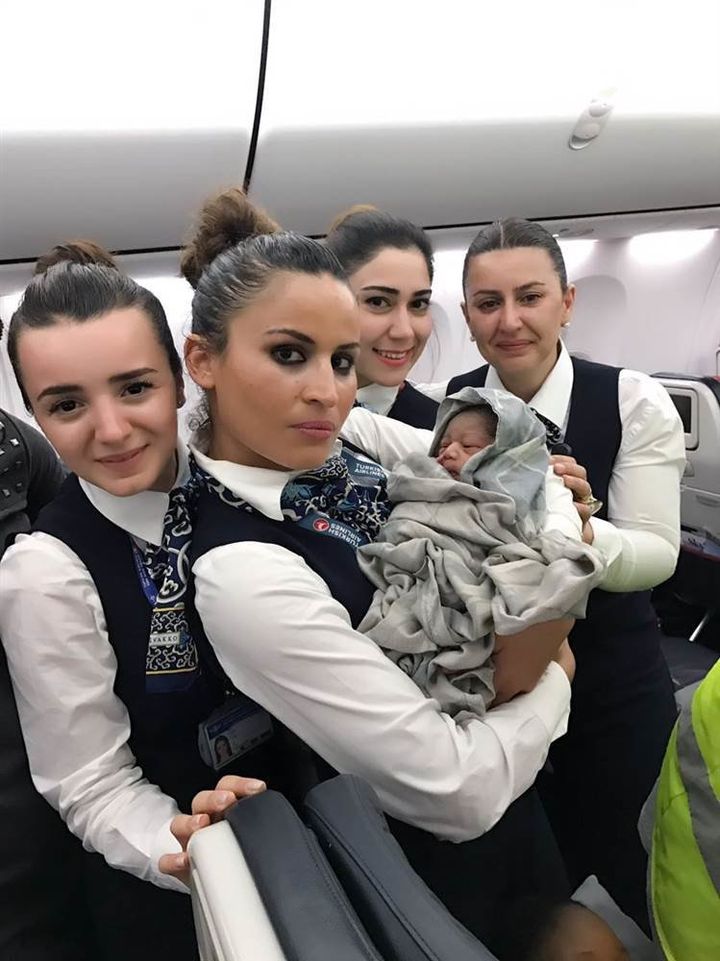 Four members of Turkish Airlines staff are seen welcoming an unexpected passenger following a mid-flight delivery.