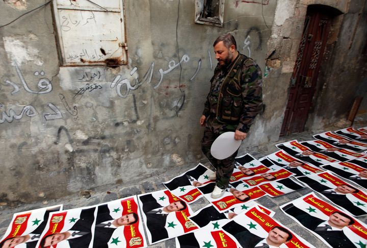 A rebel fighter walks on posters depicting Assad with writing on. It translates to 'We love you, father of Hafez'
