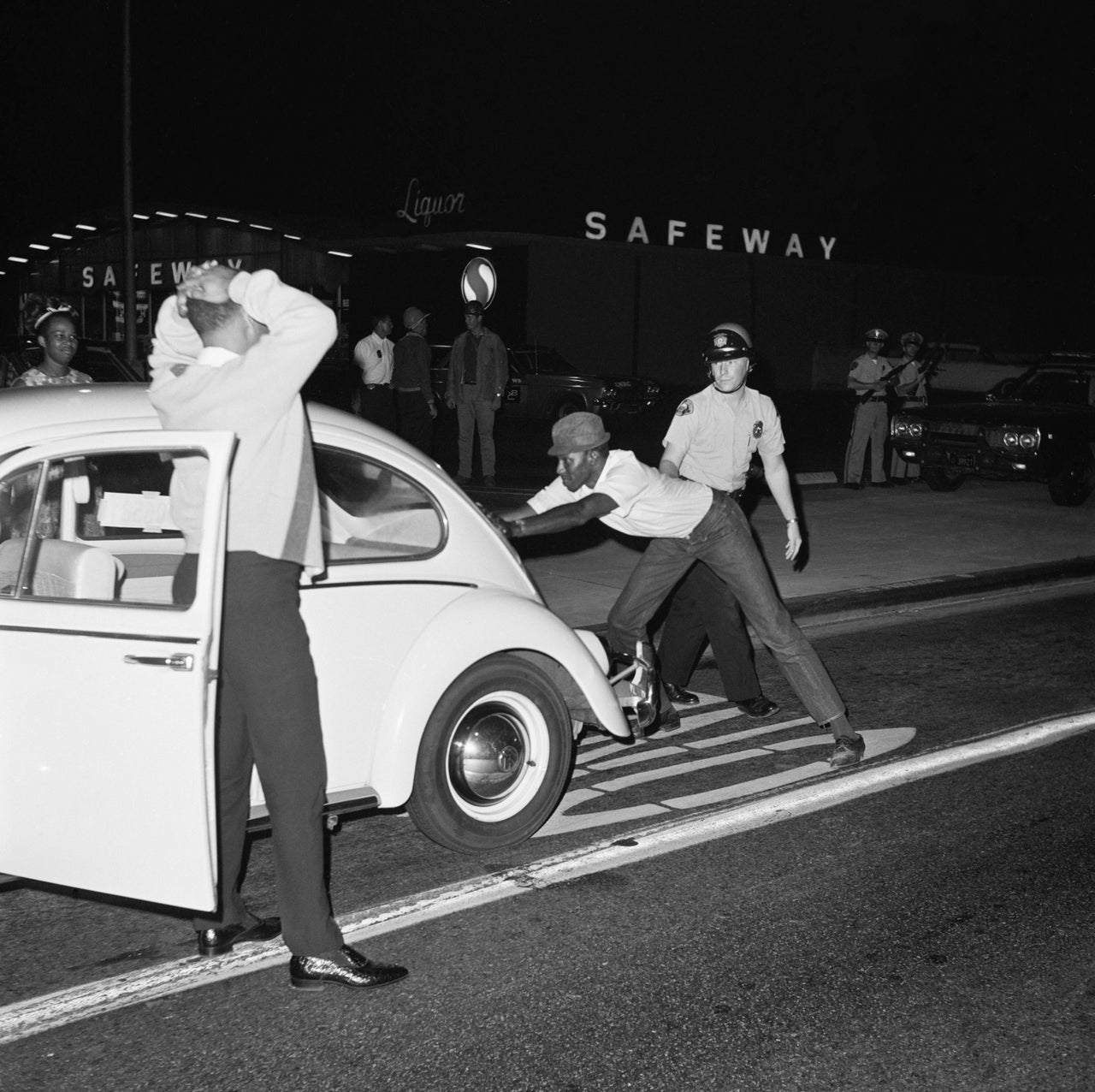 A Long Beach police officer searches black drivers and passengers for weapons at a checkpoint during the Watts Rebellion in nearby Los Angeles.