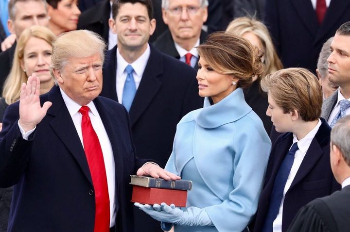 Donald Trump places his hand on a Bible and swears to uphold and defend the Constitution, as Mitch McConnell and Paul Ryan look on.