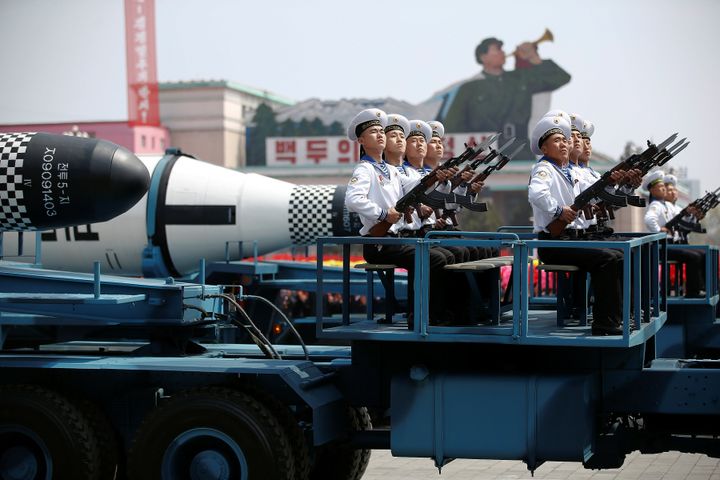 Soldiers with guns at the ready sit atop the missile laden trucks