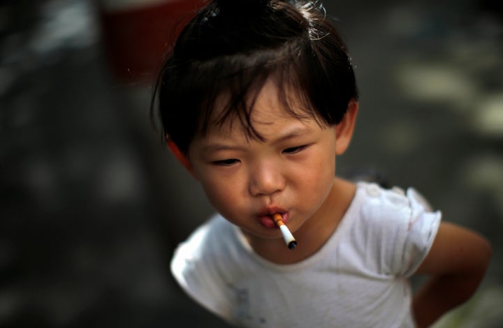 A girl stands on a sidewalk after putting an unlit cigarette in her mouth, which she picked up from the ground, in Shanghai J