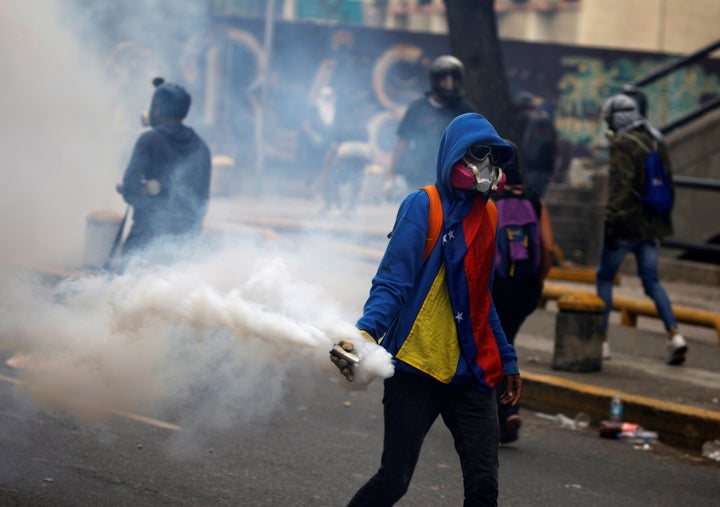 An opposition demonstrator carries a gas grenade while clashing with riot police during the so called "mother of all marches."