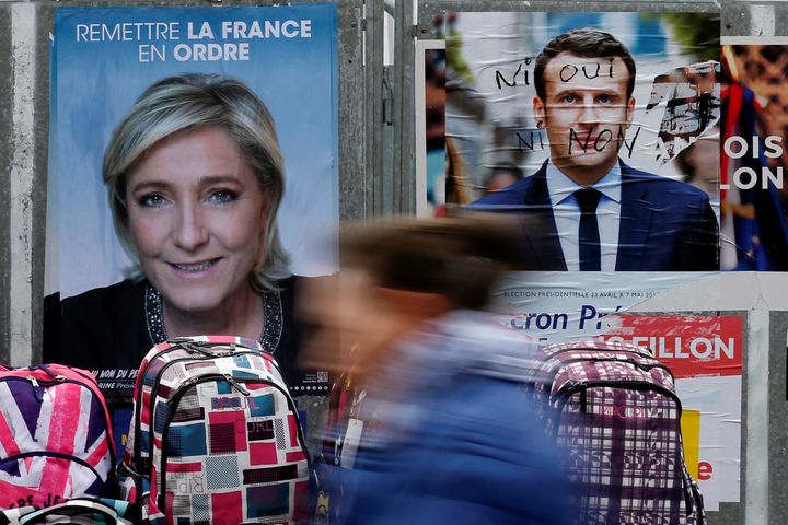A woman walks past official posters of candidates for the 2017 French presidential election, Marine Le Pen and Emmanuel Macron.