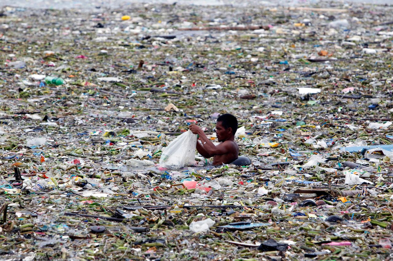 A man collects plastic and other recyclable materials from debris in the waters of Manila Bay in Manila, Philippines, July 30, 2012. Mismanaged waste from land is the primary cause of the ocean plastics crisis. 