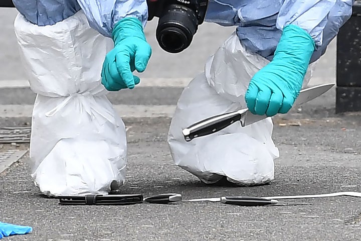 A forensic officer holds up a large knife among items left on the ground after an incident on Whitehall