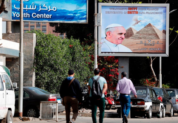 Egyptians walk past a billboard depicting Pope Francis, a few hours before his visit commences on April 28, 2017.