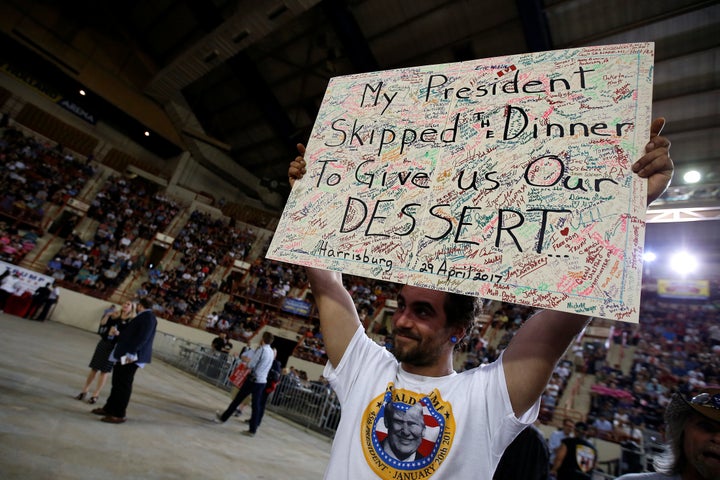 A man holds up a sign about the White House Correspondents' Dinner before a Trump rally in Harrisburg, Pennsylvania.