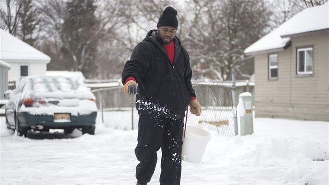 Ontayveis Underwood sprinkles salt after clearing snow from a neighbor’s driveway and sidewalk in Saginaw, Michigan. Many states and cities are educating people on how much salt to use.