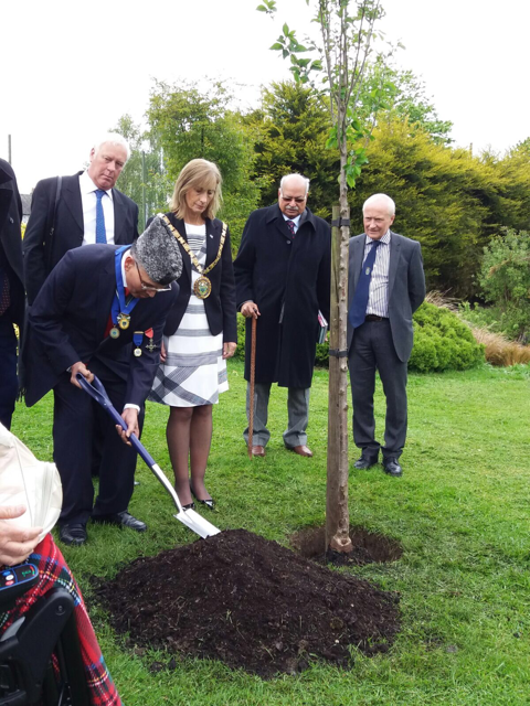 Shera, while wearing a Pakistani Jinnah cap, plants a friendship tree in the borough of Rugby at a 2017 ceremony conferring him with the honor "Freedom of the Borough of Rugby" for his dedication to the borough and to building bridges. A delegation, including former Pakistani High Commissioner Wajid Shamsul Hasan, looks on. 