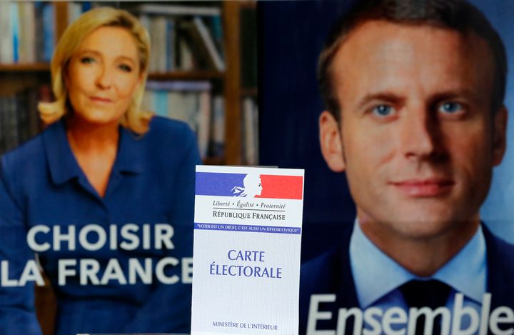 A French voter registration card is seen in front of official campaign posters of candidates in the French presidential election, Marine Le Pen (L) and Emmanuel Macron.