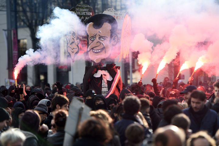 Protesters hold flares and a cardboard cutout of Macron aloft during protests in he lead-up to the elections