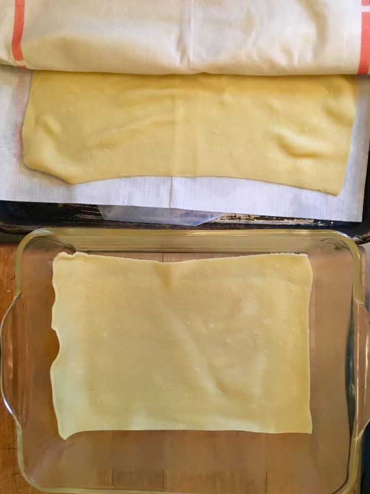 The first layer of blanched pasta in a buttered oven dish