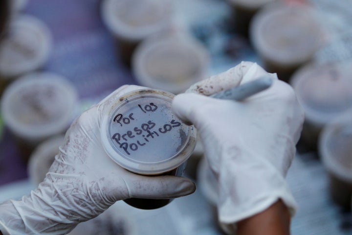 A woman writes a text that reads "For the political prisoners" on a plastic pot filled with feces.