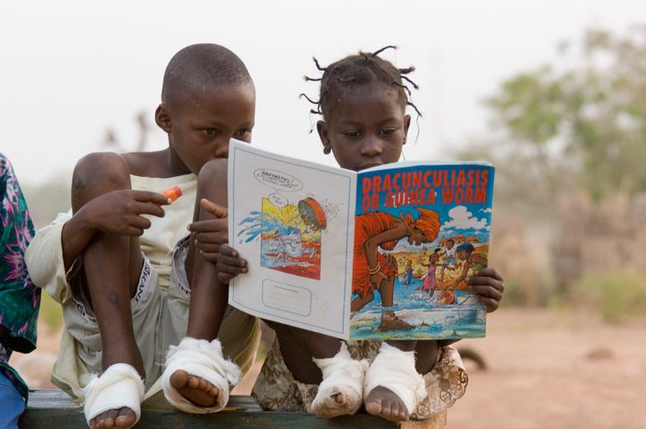 Two children, whose feet were bandaged after being treated for Guinea worm, look at an illustrated book about the disease.