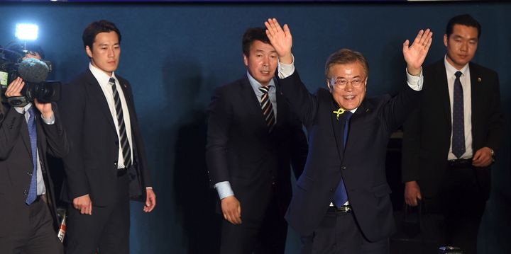 Moon Jae-in waves his hands as his bodyguards look on. 