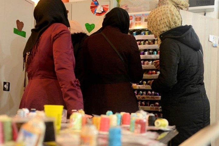 Syrian women stand in front of a selection of threads at a workshop with Drop Earrings, Not Bombs.