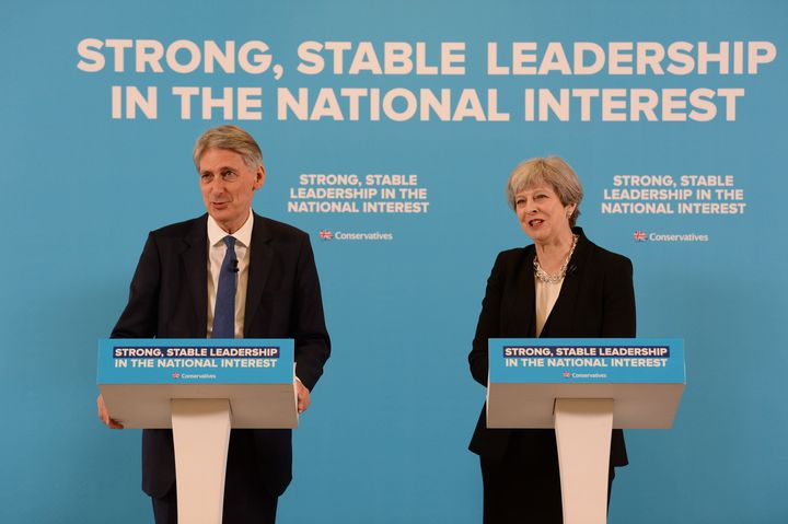 Theresa May and Philip Hammond speaking in front of a subtle campaign message.