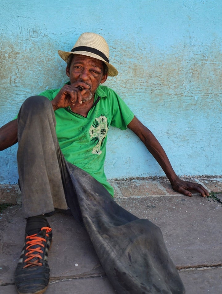 <p>A man sits outside catching a breeze and enjoying a Cuban cigar in Trinidad</p>