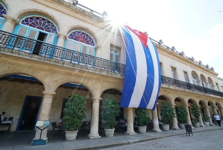 <p>The sun glows bright behind the Cuban flag in Old Havana</p>