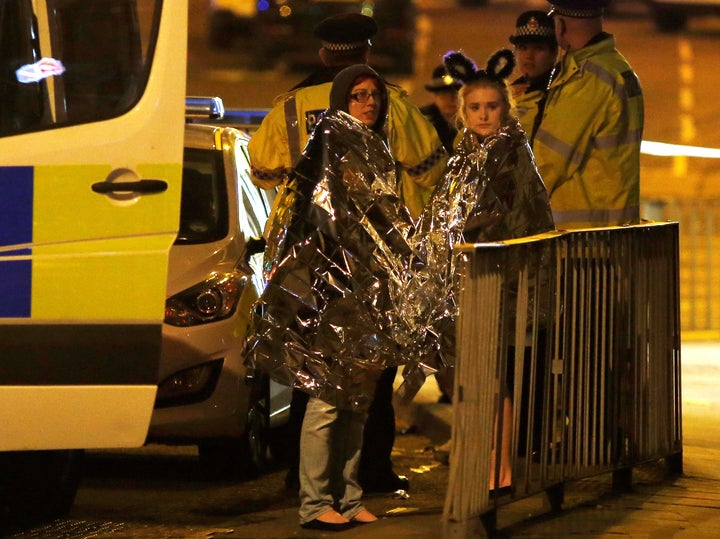 Two women wrapped in formal blankets stand near the Manchester Area where a lone male attacker detonated a bomb, killing 22