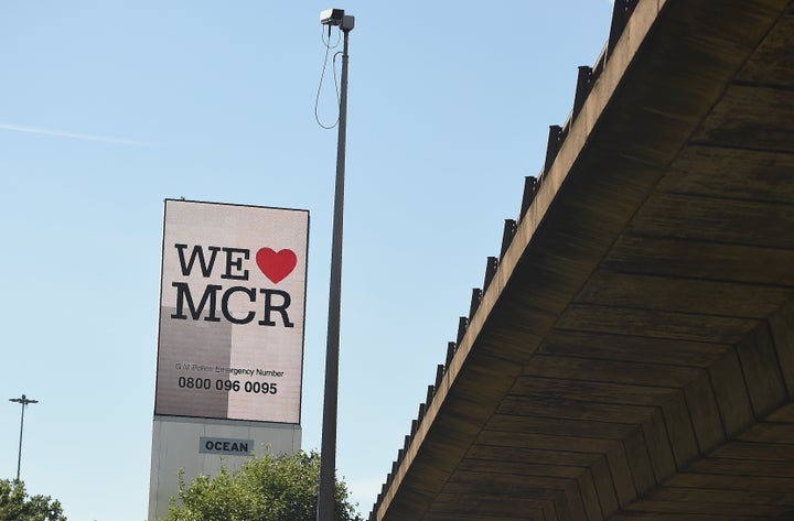 An electronic advertising board displays a "We love MCR" sign, along with a telephone number for Greater Manchester Police, n