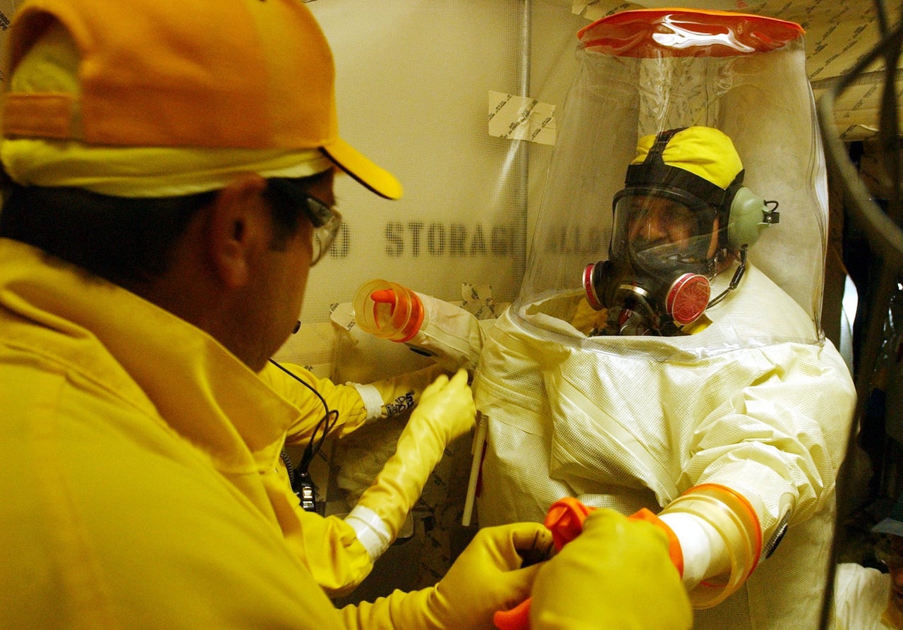 Rocky Flats workers help Thomas Chevarria put on his anti-contamination suit before entering the "infinity room" area in Building 771.