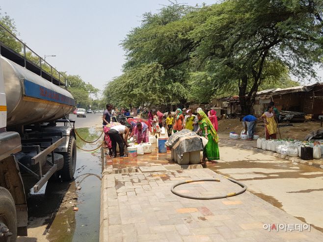 The water tanker (left) run by the Delhi government is silver-colored with the Delhi government agency logo on it. The photo shows the residents of Tughlakabad receiving water for the first time in ten days./ Photographed by Jeong In-seo 