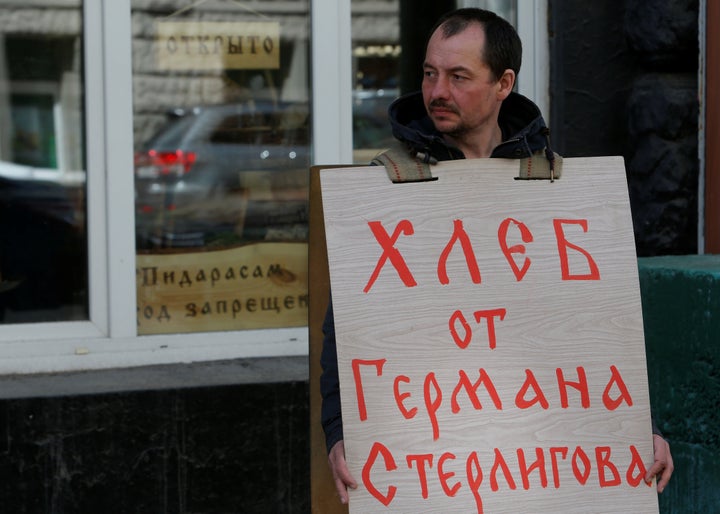 A man holds a placard advertising the German Sterligov's food store next to the shop's entrance with a plate which reads "No entry for faggots."