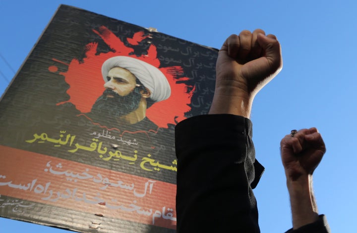 Iranian protesters raise their fists in front of a portrait of prominent Shiite Muslim cleric Nimr al-Nimr during a demonstra