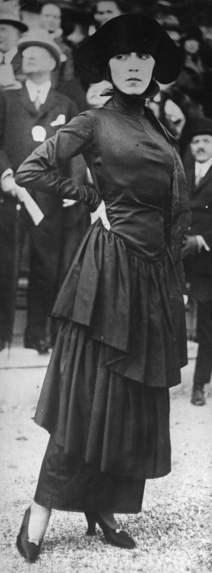 A Poiret model wearing a dress of black marocain with a severe neckline and flounced hobble skirt.