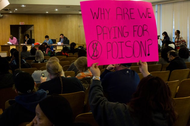 A woman holds a sign criticizing water costs at a Flint City Council meeting in