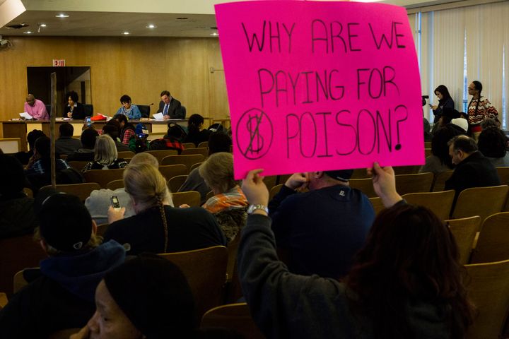 A woman holds a sign criticizing water costs at a Flint City Council meeting in February.