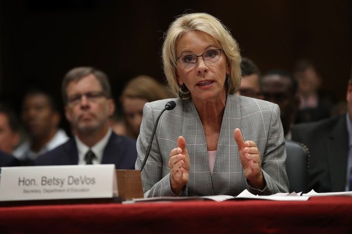 Secretary of Education Betsy DeVos testifies before the Senate Appropriations Committee on June 6th, 2017. She is wearing a grey blazer and is leaning into her microphone.