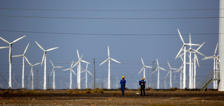 Workers walk near wind turbines for generating electricity, at a wind farm in Guazhou, China.